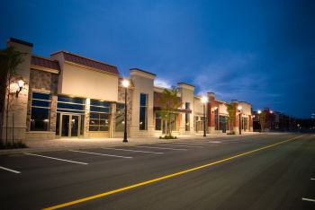 Empty shopping center storefronts lit at dusk along a quiet road